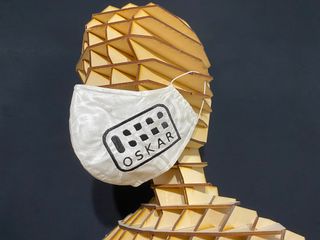 Mundnasenschutz mit schwarz auf weiß gesticktem Oskar Logo. Der Mundnasenschutz wird von einem Schnittmodell-Kopf aus Pappelsperrholz getragen.
